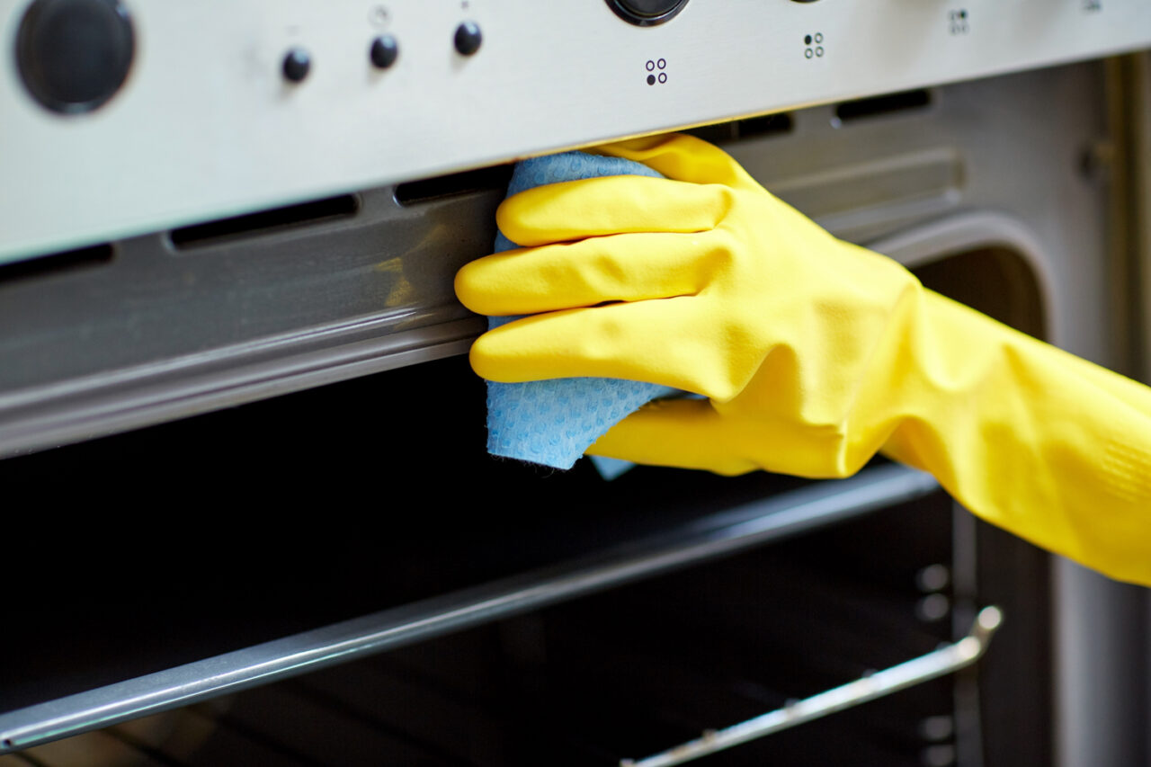 Mujer manos en guantes con botella de detergente cocina horno de